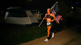 Meg Eckert runs at night with American flag after setting women’s 6-day world record.