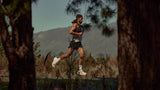 Luke Nelson running outdoors with a pair of Mount to Coast shoes on a trail surrounded by trees and mountains.